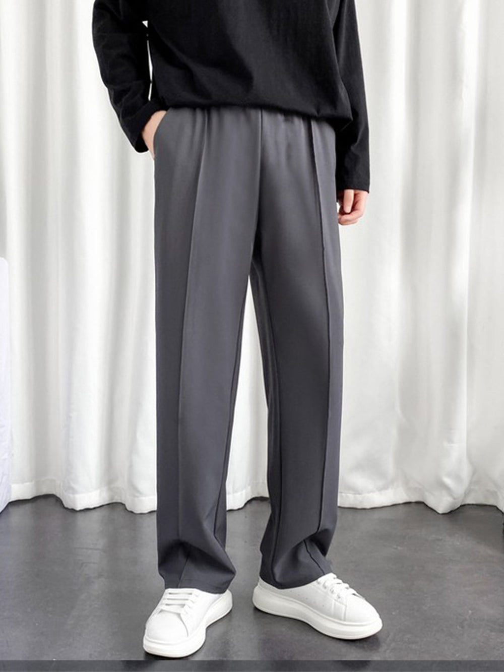 Model wearing men's charcoal baggy joggers with elastic waist and front crease paired with white sneakers and black top