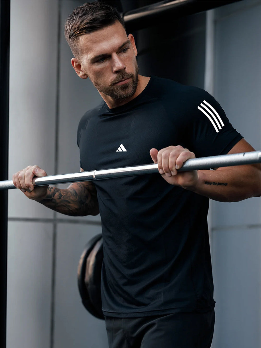 URBAN WOLFS model lifting barbell in men's dry-fit black tees, fitted moisture-wicking workout shirt with sleeve stripes