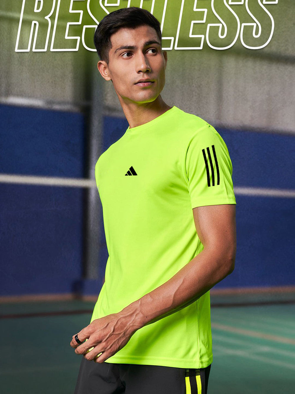 Male model wearing men's lime green dri-fit t-shirt with black logo and sleeve stripes on indoor court