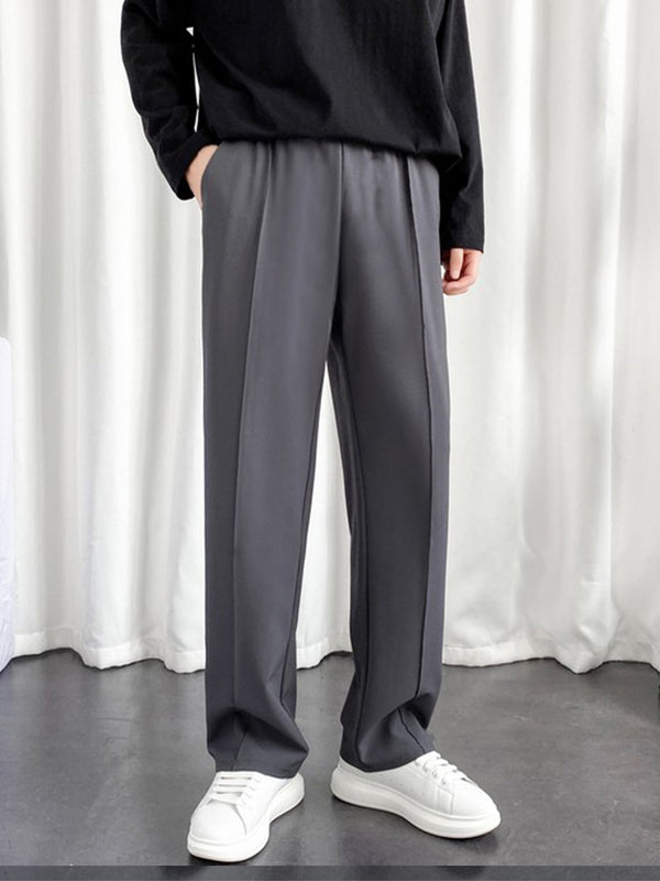 Model wearing men's charcoal baggy joggers with elastic waist and front crease paired with white sneakers and black top
